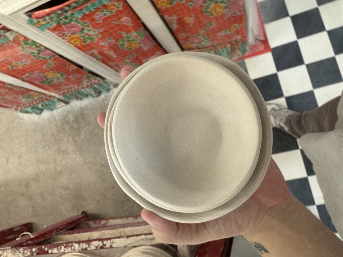 A stack of just-thrown ceramic bowls held over a studio floor