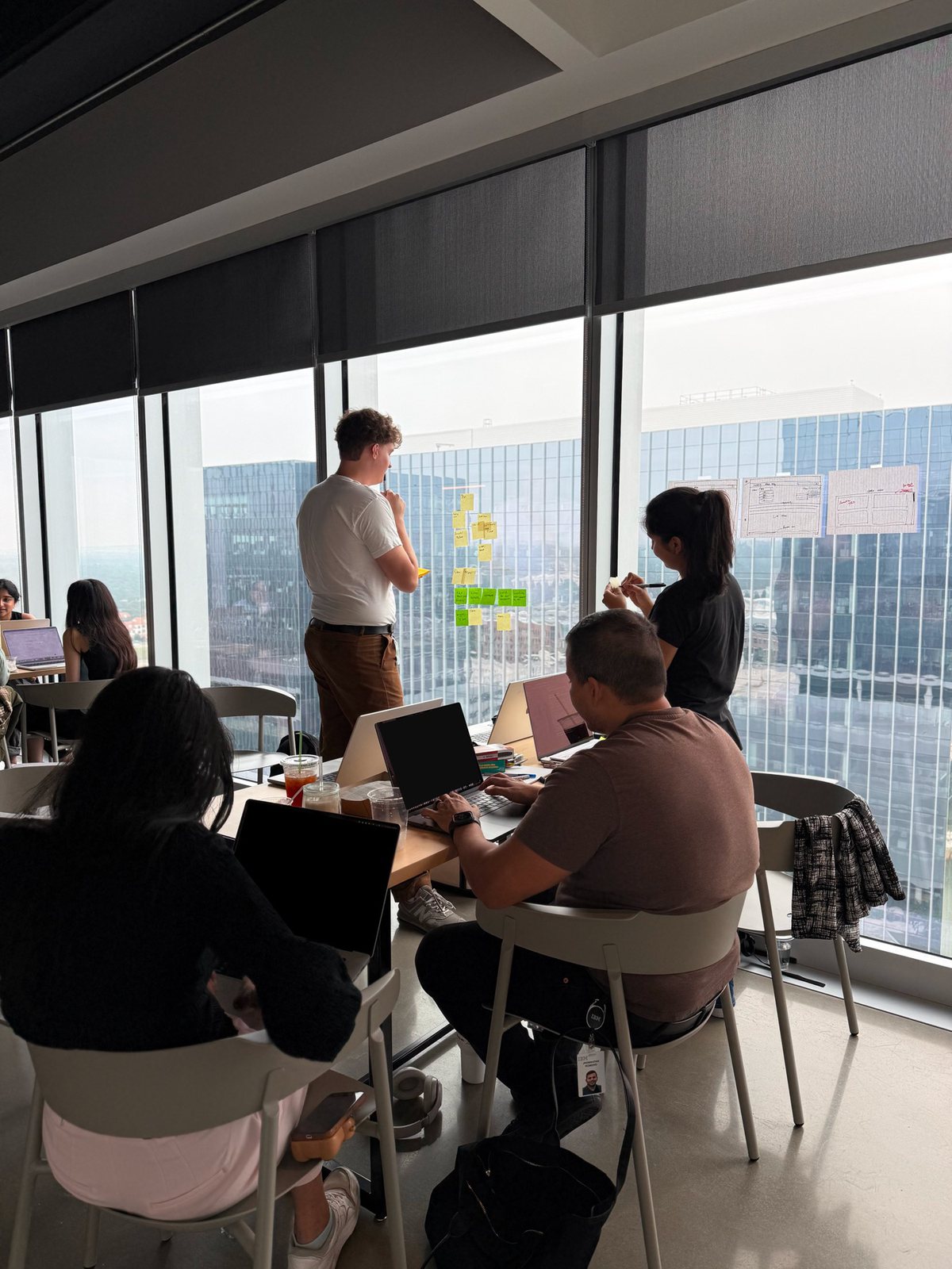 A design team working around a table in a high-rise office, sticky notes on the window