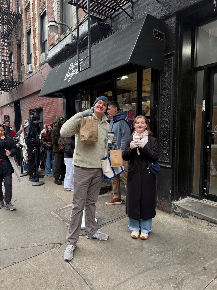 Brayden and a friend outside a bagel shop in New York, holding coffee and paper bags